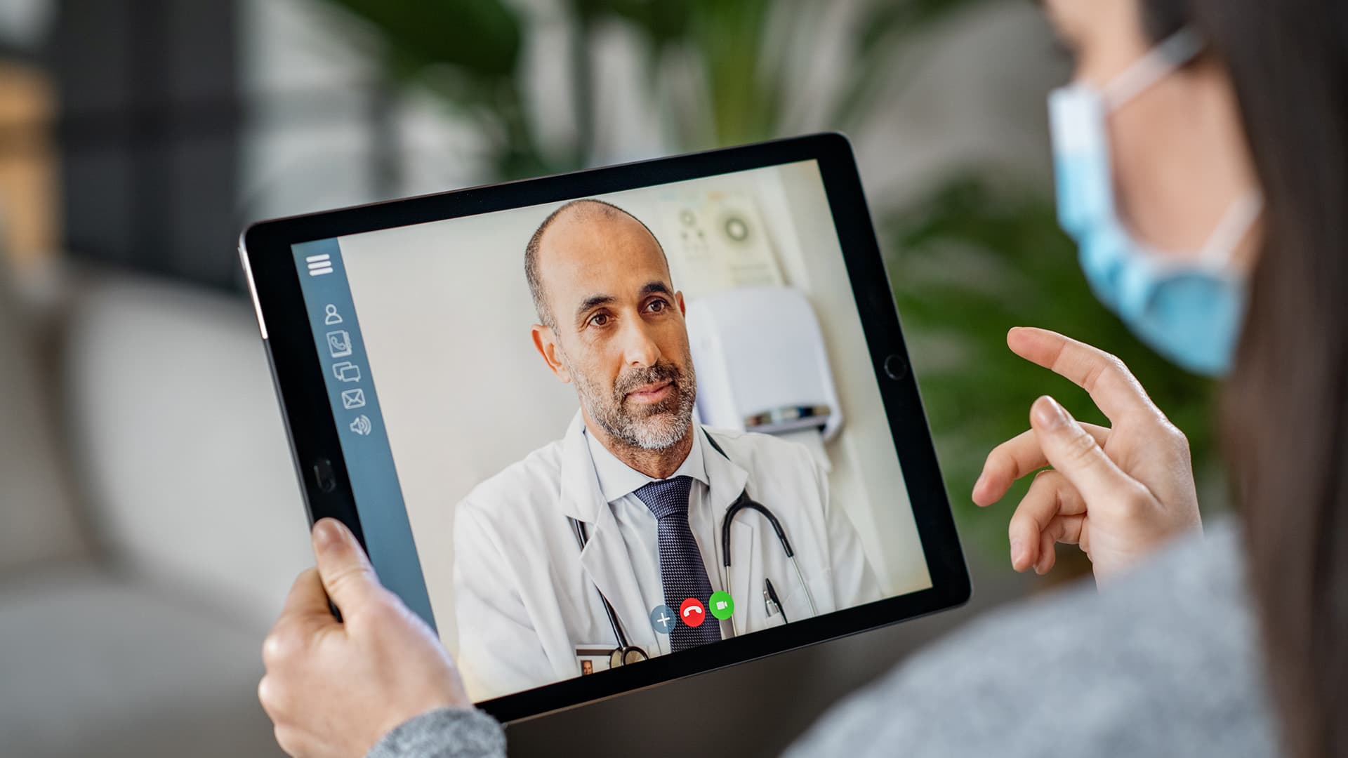 young patient wearing a mask having a video conference with her doctor online