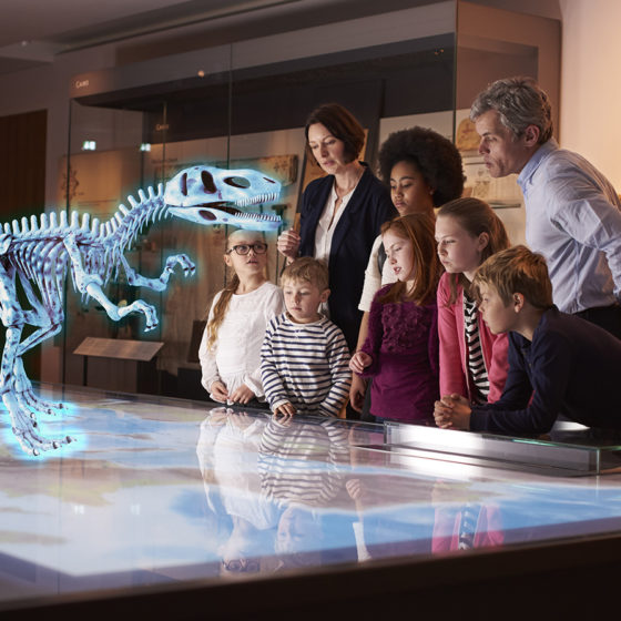 group of people at museum seeing dinosaur hologram on a map