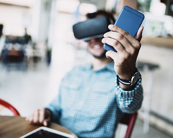 Young handsome man sitting in cyber cafe and using virtual reality headset or glasses